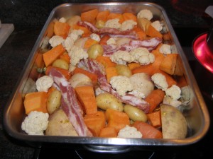 On répartit les légumes en une couche dans un grand plat à four et on insère les tranches de poitrine de porc, verticalement et couenne vers le bas.